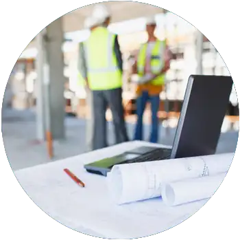 A laptop is on a table with blueprints at a construction site.